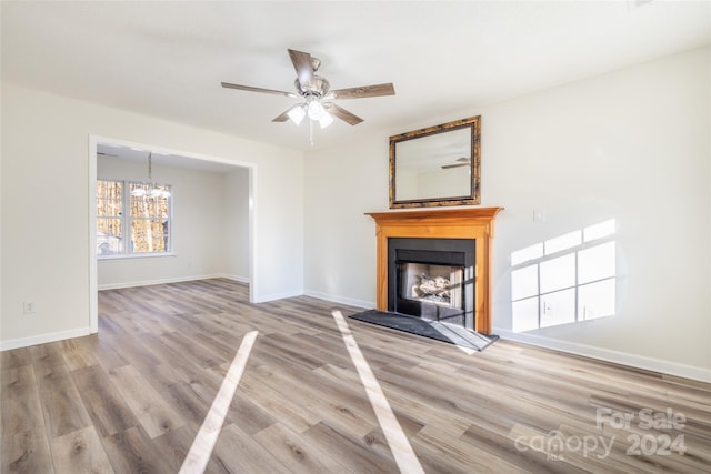 unfurnished living room featuring ceiling fan with notable chandelier and light hardwood / wood-style flooring