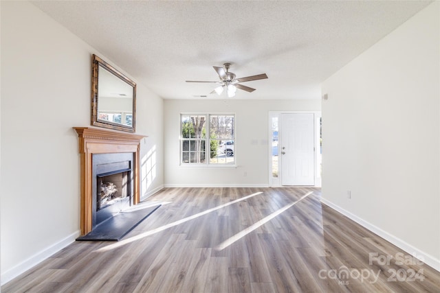 unfurnished living room featuring ceiling fan, light hardwood / wood-style flooring, and a textured ceiling