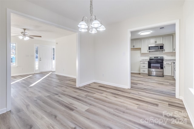 unfurnished dining area with ceiling fan with notable chandelier and light hardwood / wood-style flooring