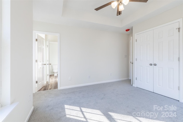 unfurnished bedroom featuring light carpet, a closet, a tray ceiling, and ceiling fan