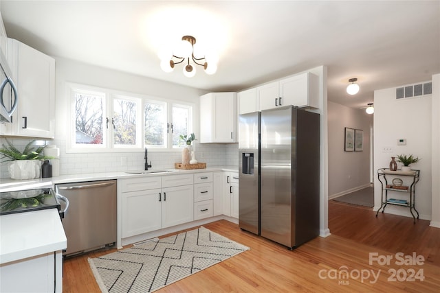 kitchen with decorative backsplash, appliances with stainless steel finishes, sink, light hardwood / wood-style floors, and white cabinetry