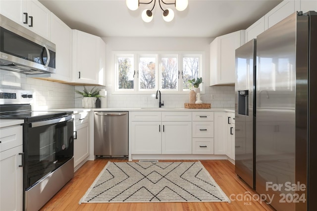 kitchen with decorative backsplash, white cabinetry, stainless steel appliances, and light hardwood / wood-style flooring