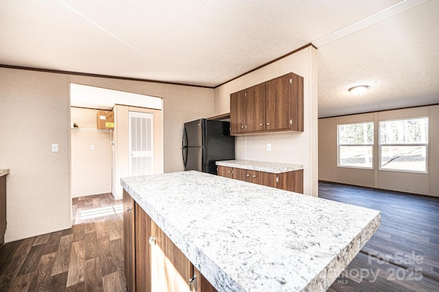 kitchen with crown molding, a textured ceiling, black refrigerator, dark hardwood / wood-style floors, and a kitchen island