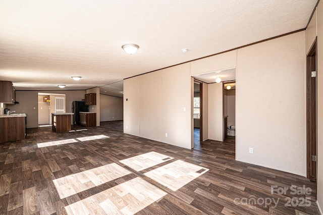 unfurnished living room featuring crown molding, dark hardwood / wood-style floors, sink, and a textured ceiling