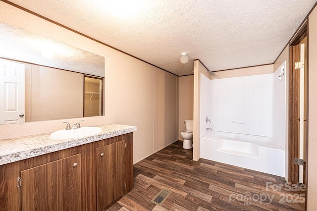 full bathroom with wood-type flooring, vanity, toilet, a textured ceiling, and washtub / shower combination