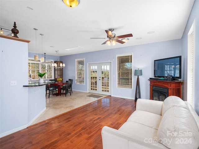 living room featuring french doors, ceiling fan with notable chandelier, and light hardwood / wood-style floors