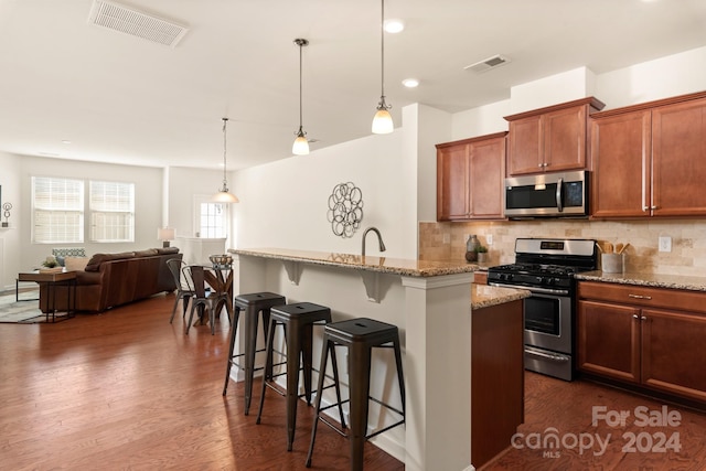 kitchen with light stone counters, stainless steel appliances, dark wood-type flooring, hanging light fixtures, and a breakfast bar area