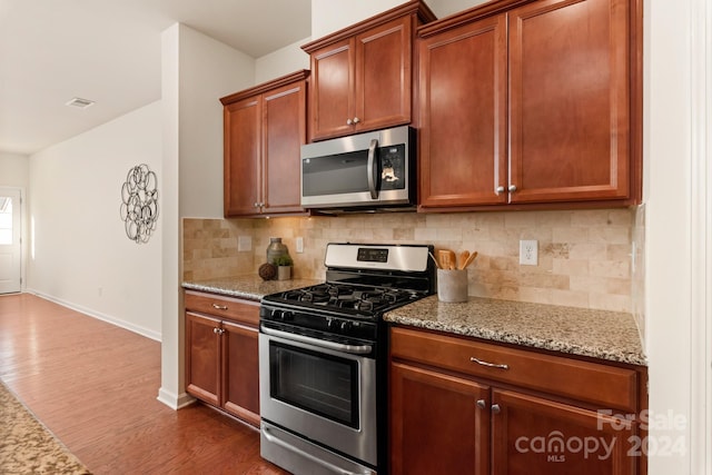 kitchen featuring decorative backsplash, light stone counters, dark hardwood / wood-style flooring, and stainless steel appliances