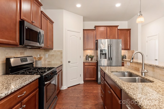 kitchen featuring appliances with stainless steel finishes, light stone counters, sink, pendant lighting, and dark hardwood / wood-style floors