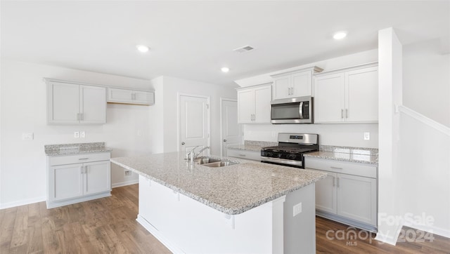 kitchen with hardwood / wood-style floors, sink, an island with sink, white cabinetry, and stainless steel appliances