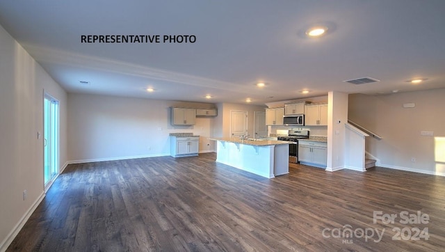 kitchen with appliances with stainless steel finishes, a wealth of natural light, dark wood-type flooring, sink, and an island with sink