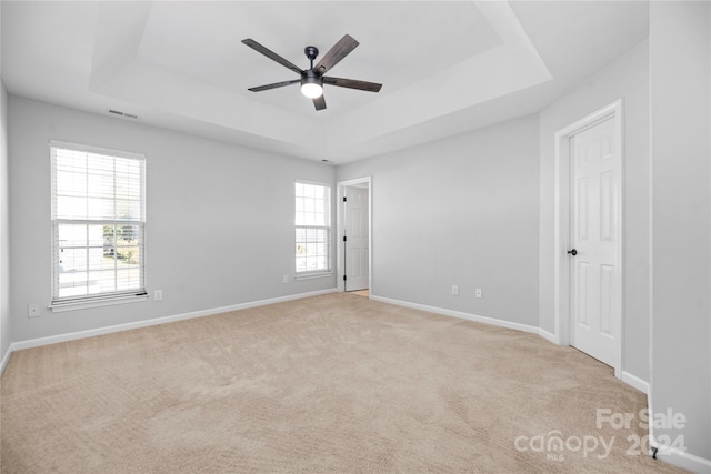 spare room with light colored carpet, a raised ceiling, and ceiling fan