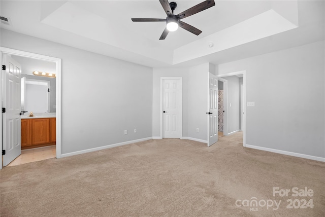 unfurnished bedroom with light carpet, ensuite bathroom, a raised ceiling, and ceiling fan