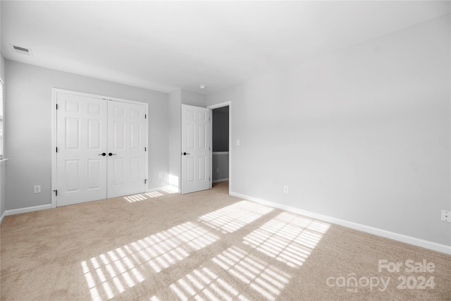 unfurnished bedroom with light carpet and a closet