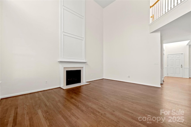 unfurnished living room with hardwood / wood-style floors and a towering ceiling