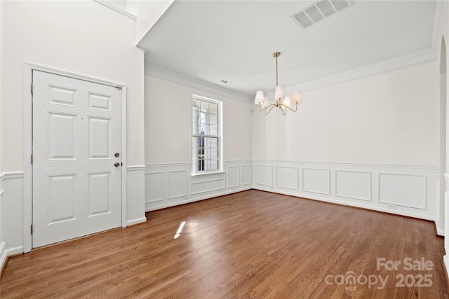 unfurnished dining area featuring hardwood / wood-style flooring, ornamental molding, and a notable chandelier