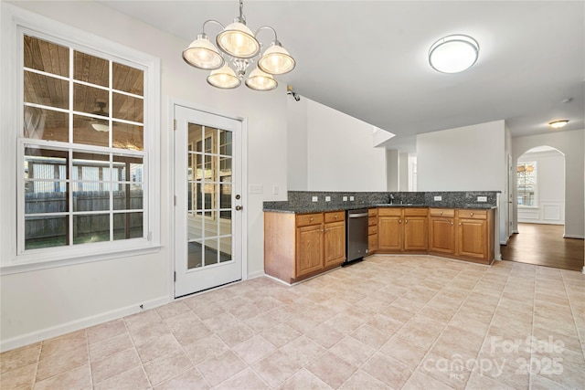 kitchen with stainless steel dishwasher, sink, pendant lighting, an inviting chandelier, and dark stone countertops