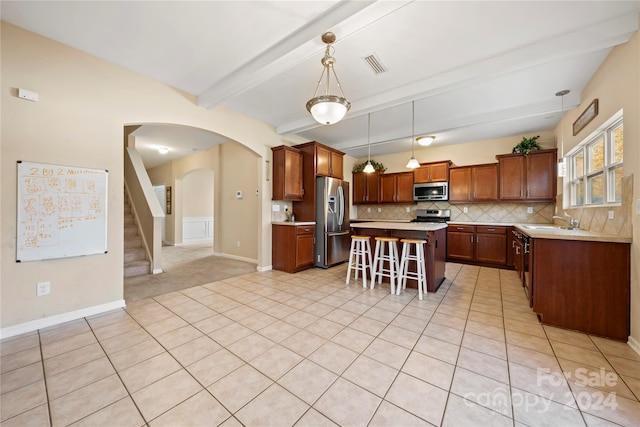 kitchen featuring a kitchen breakfast bar, tasteful backsplash, beamed ceiling, a kitchen island, and appliances with stainless steel finishes