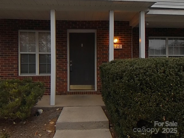 doorway to property featuring covered porch and brick siding