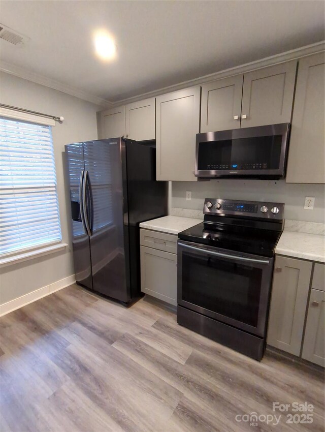 kitchen with gray cabinets, appliances with stainless steel finishes, light countertops, and ornamental molding