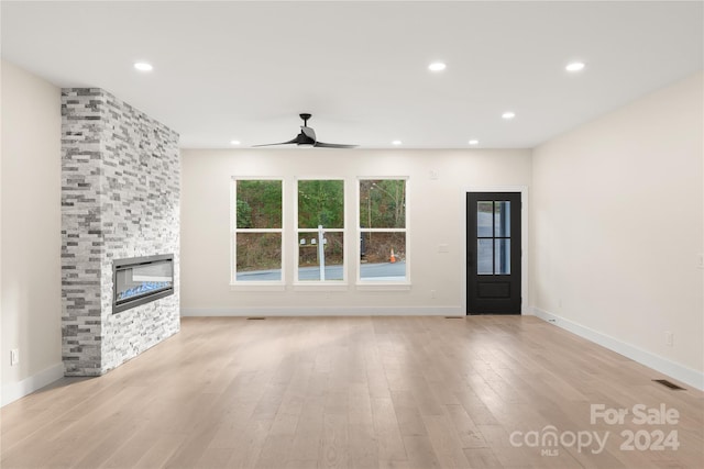 unfurnished living room with ceiling fan, a stone fireplace, and light hardwood / wood-style flooring