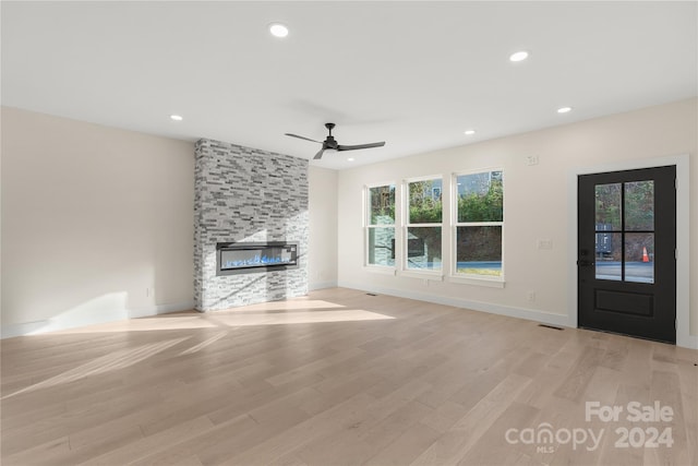 unfurnished living room with a large fireplace, light hardwood / wood-style flooring, and ceiling fan