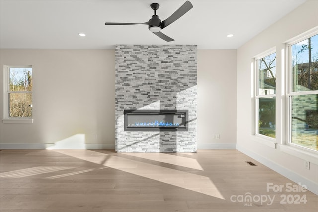 unfurnished living room with ceiling fan, a fireplace, and light wood-type flooring