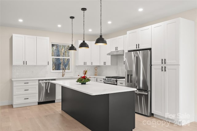 kitchen with decorative light fixtures, a kitchen island, light wood-type flooring, and appliances with stainless steel finishes