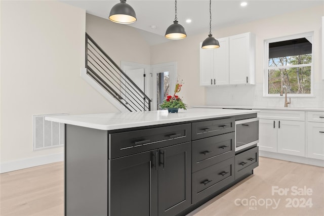 kitchen featuring a center island, white cabinets, sink, decorative light fixtures, and light hardwood / wood-style floors