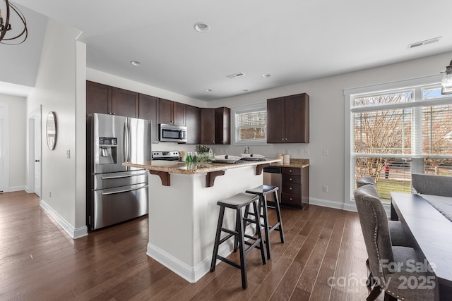 kitchen featuring appliances with stainless steel finishes, a breakfast bar, dark brown cabinets, a center island, and dark hardwood / wood-style floors