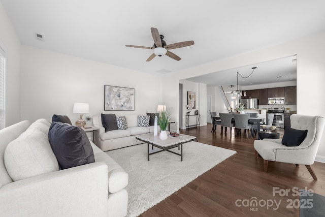 living room with dark hardwood / wood-style flooring and ceiling fan with notable chandelier