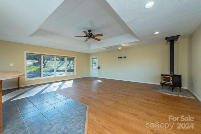 208 Dogwood Ln, Black Mountain, NC 28711 - unfurnished living room featuring a wood stove, ceiling fan, a textured ceiling, a tray ceiling, and wood-type flooring