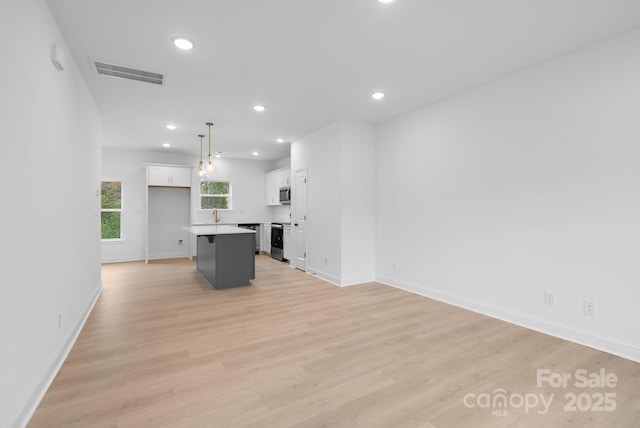 kitchen with light wood-type flooring, a kitchen island, pendant lighting, stainless steel appliances, and white cabinets