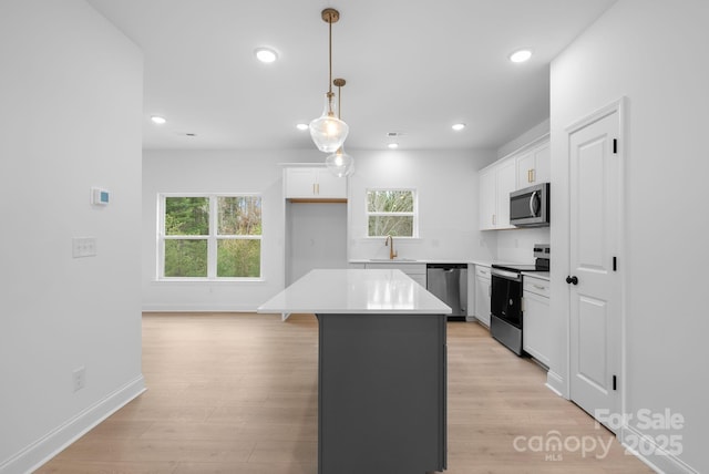 kitchen featuring a center island, light wood-type flooring, appliances with stainless steel finishes, pendant lighting, and white cabinets