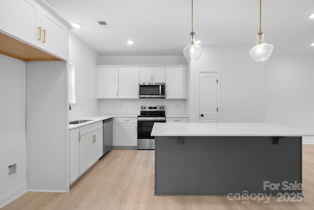 kitchen featuring decorative light fixtures, light hardwood / wood-style flooring, white cabinets, and appliances with stainless steel finishes