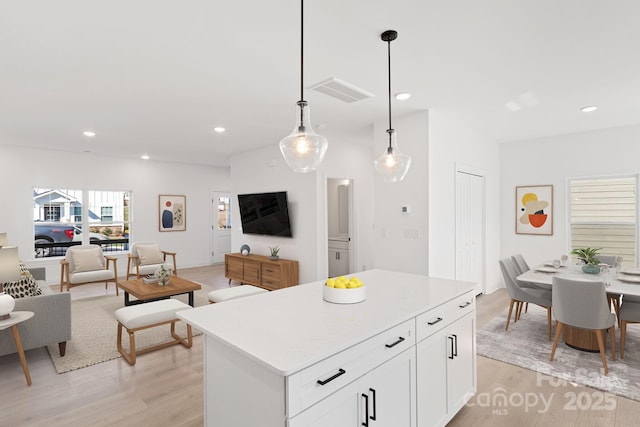 kitchen featuring decorative light fixtures, a center island, light hardwood / wood-style flooring, and white cabinets