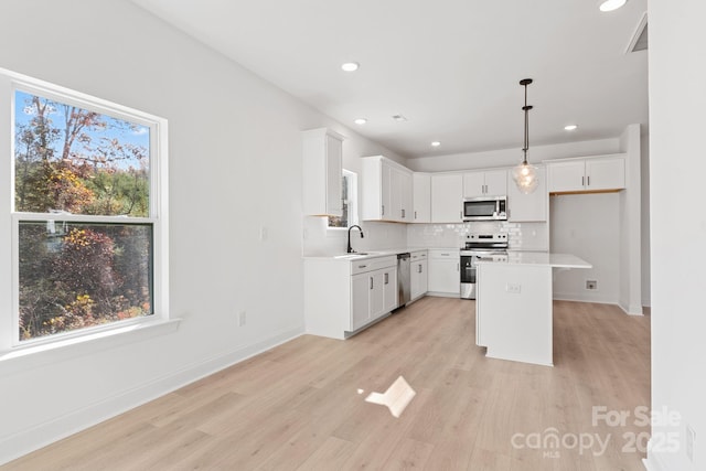 kitchen with a kitchen island, decorative light fixtures, white cabinetry, sink, and stainless steel appliances