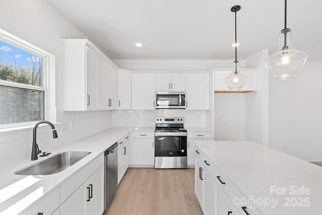 kitchen with sink, pendant lighting, stainless steel appliances, light hardwood / wood-style floors, and white cabinets