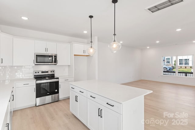 kitchen with a kitchen island, appliances with stainless steel finishes, decorative light fixtures, white cabinetry, and light wood-type flooring