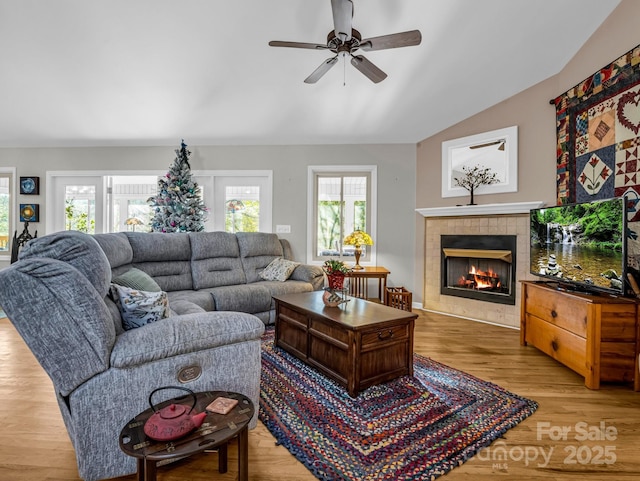 living room with a tile fireplace, vaulted ceiling, ceiling fan, and light hardwood / wood-style flooring