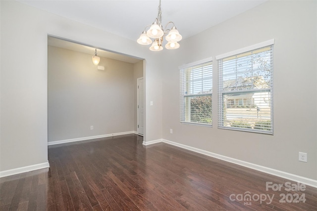 spare room with a wealth of natural light, a chandelier, and dark hardwood / wood-style floors