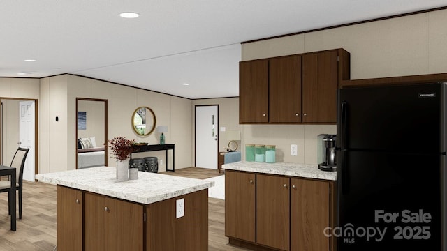 kitchen featuring dark brown cabinets, light wood-type flooring, black fridge, and a kitchen island