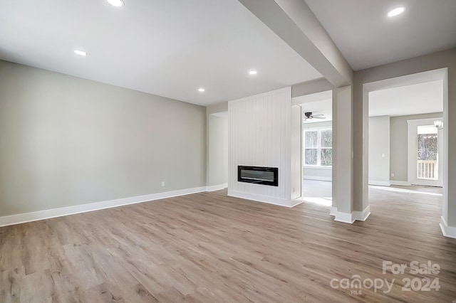 unfurnished living room with heating unit, ceiling fan, a large fireplace, and light hardwood / wood-style floors