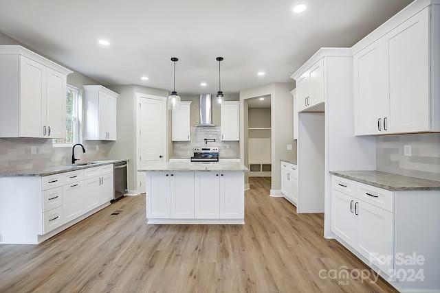 kitchen featuring wall chimney range hood, a kitchen island, appliances with stainless steel finishes, light hardwood / wood-style floors, and white cabinetry