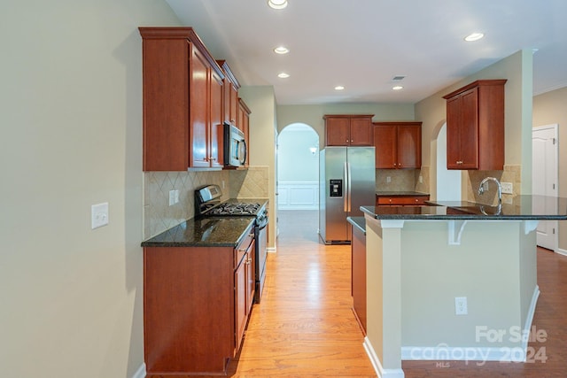 kitchen featuring dark stone counters, tasteful backsplash, light hardwood / wood-style floors, and appliances with stainless steel finishes