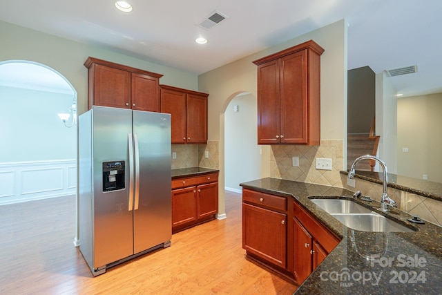 kitchen with stainless steel fridge, light wood-type flooring, dark stone counters, and sink