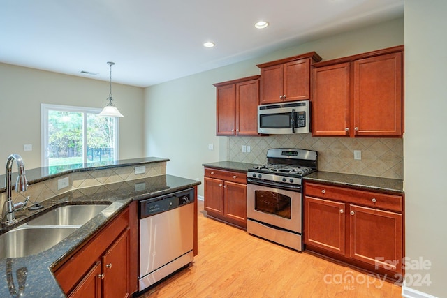 kitchen with dark stone counters, sink, appliances with stainless steel finishes, decorative light fixtures, and light hardwood / wood-style floors