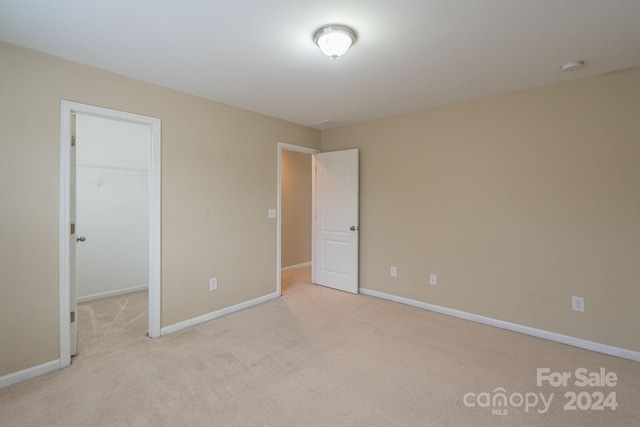 unfurnished bedroom featuring light colored carpet, a spacious closet, and a closet