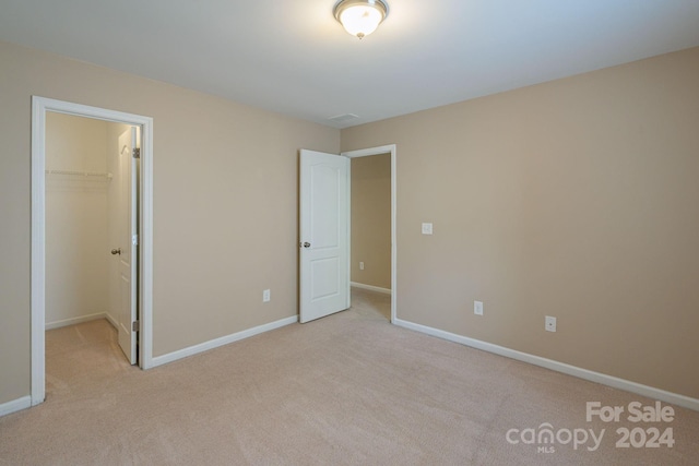 unfurnished bedroom featuring a walk in closet, light carpet, and a closet