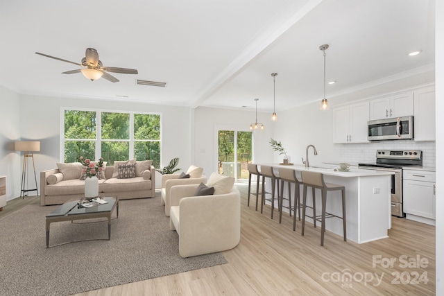 living room featuring sink, ceiling fan, light wood-type flooring, ornamental molding, and beam ceiling